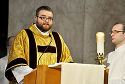 Transitional Deacon Doug Marcotte proclaims the Gospel during the archdiocese’s annual chrism Mass on March 26 at SS. Peter and Paul Cathedral in Indianapolis. He will be ordained to the priesthood on May 18. Seminarian Michael Keucher holds a candle at right. (Submitted photo/Kent Hughes)